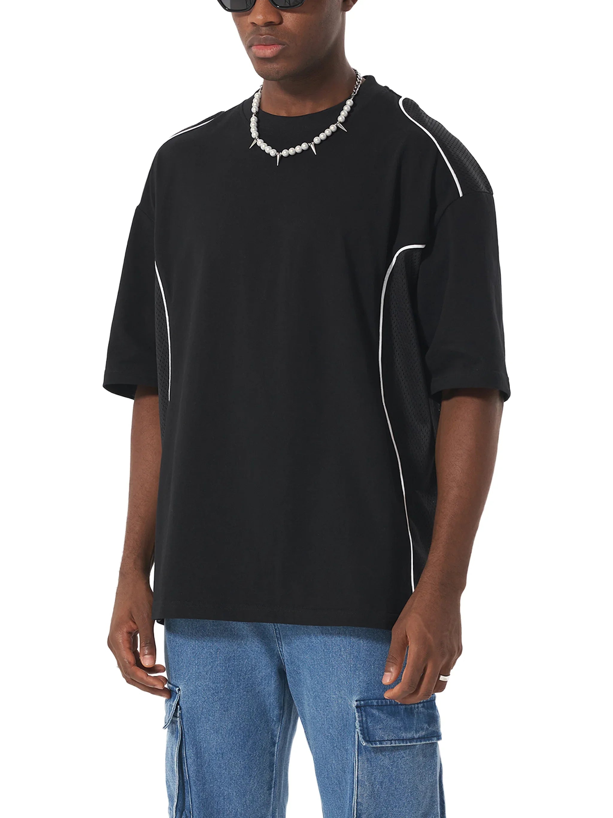 Man wearing oversized black t-shirt with white piping and blue cargo jeans, modern streetwear style