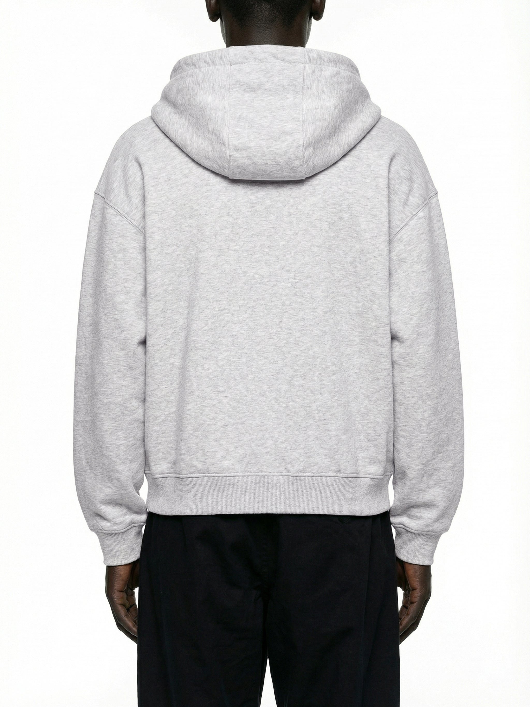 Back view of a man wearing a light grey oversized hoodie and black pants on white background